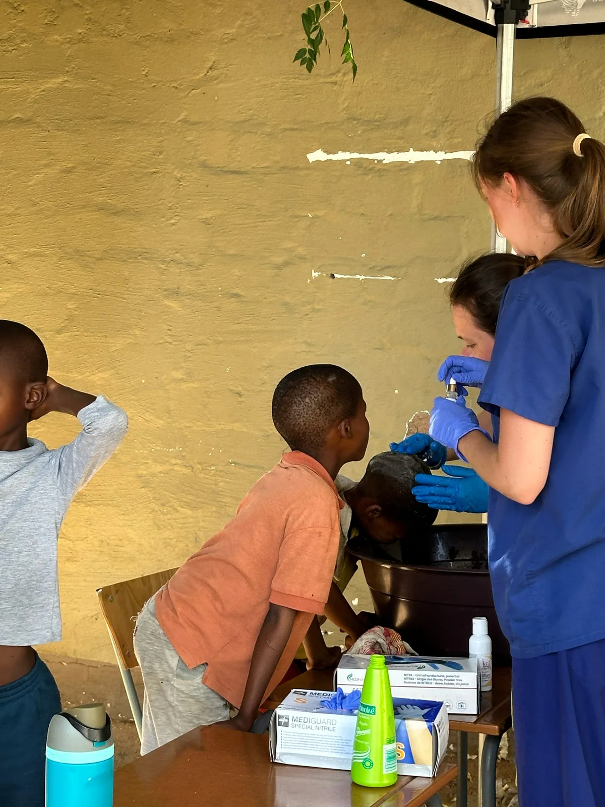 Care workers helping a child wash their hair over a basin